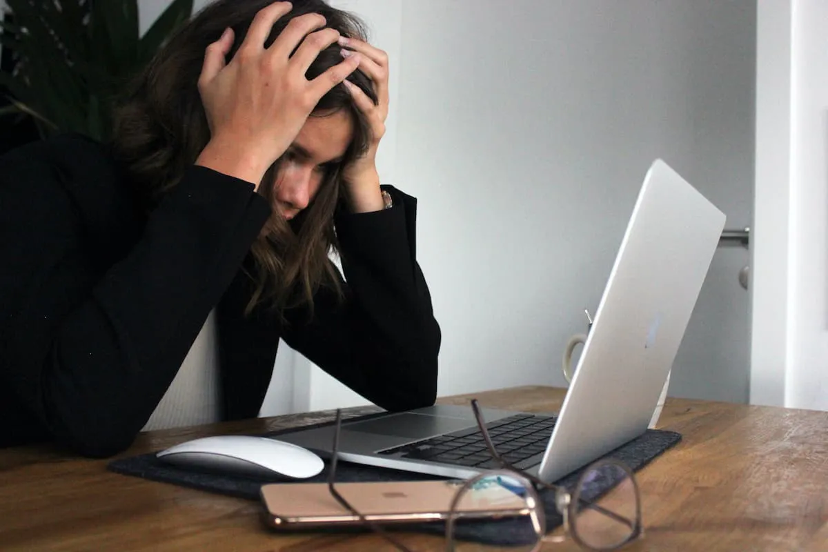 Frustrated developer looking at her laptop with her hands on her head.